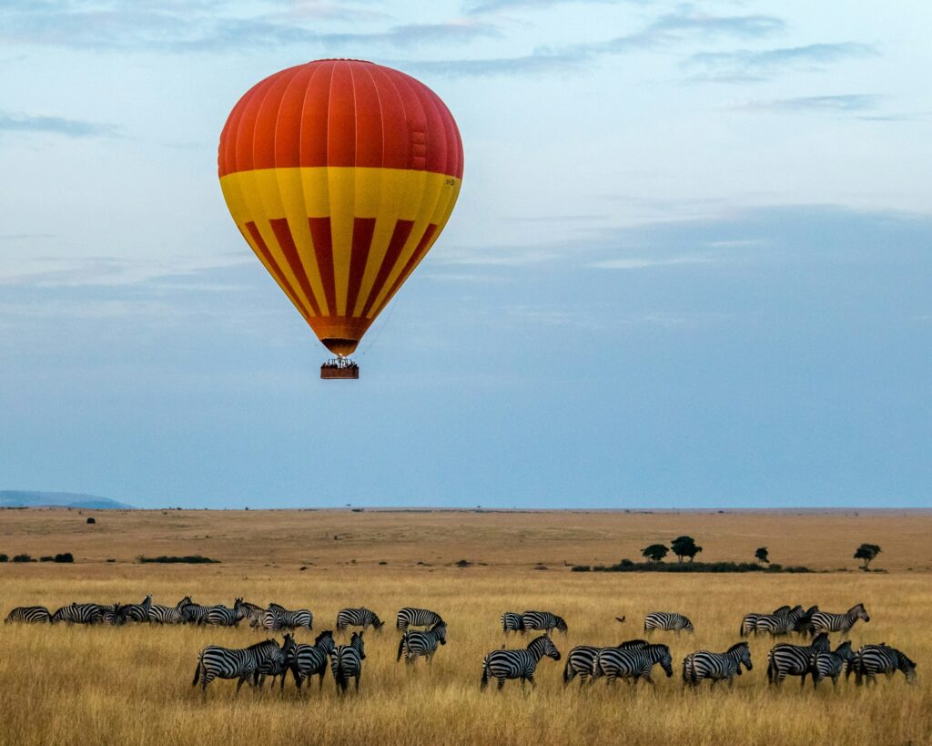 A vibrant and immersive safari tour experience in the heart of the African wilderness. In the foreground, a group of adventurous travelers embark on an open-air safari vehicle, their gazes fixed on the vast expanse of the savanna. Majestic elephants, giraffes, and other iconic wildlife roam freely in the middle ground, while in the background, a stunning panorama of rolling hills, acacia trees, and a cloudless sky create a sense of awe and tranquility. The warm, golden light of the African sun bathes the scene, casting a natural and inviting glow. The composition and attention to detail evoke the excitement and wonder of planning a safari adventure.