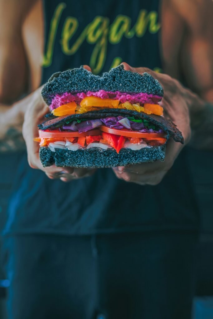 person holding meat sandwich with sliced tomatoes, onions, and grilled meat person holding meat sandwich with sliced tomatoes, onions, and grilled meat