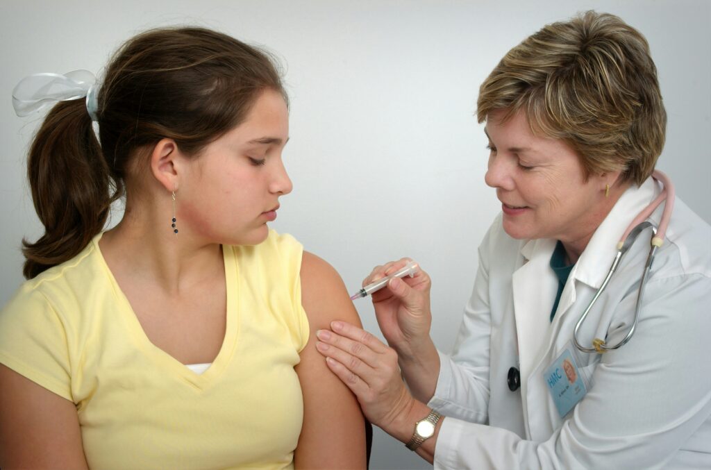 woman injecting girl's left arm woman injecting girl's left arm